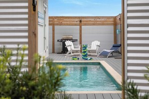 A pool area with a wooden deck, lounge chairs, and a barbecue grill.