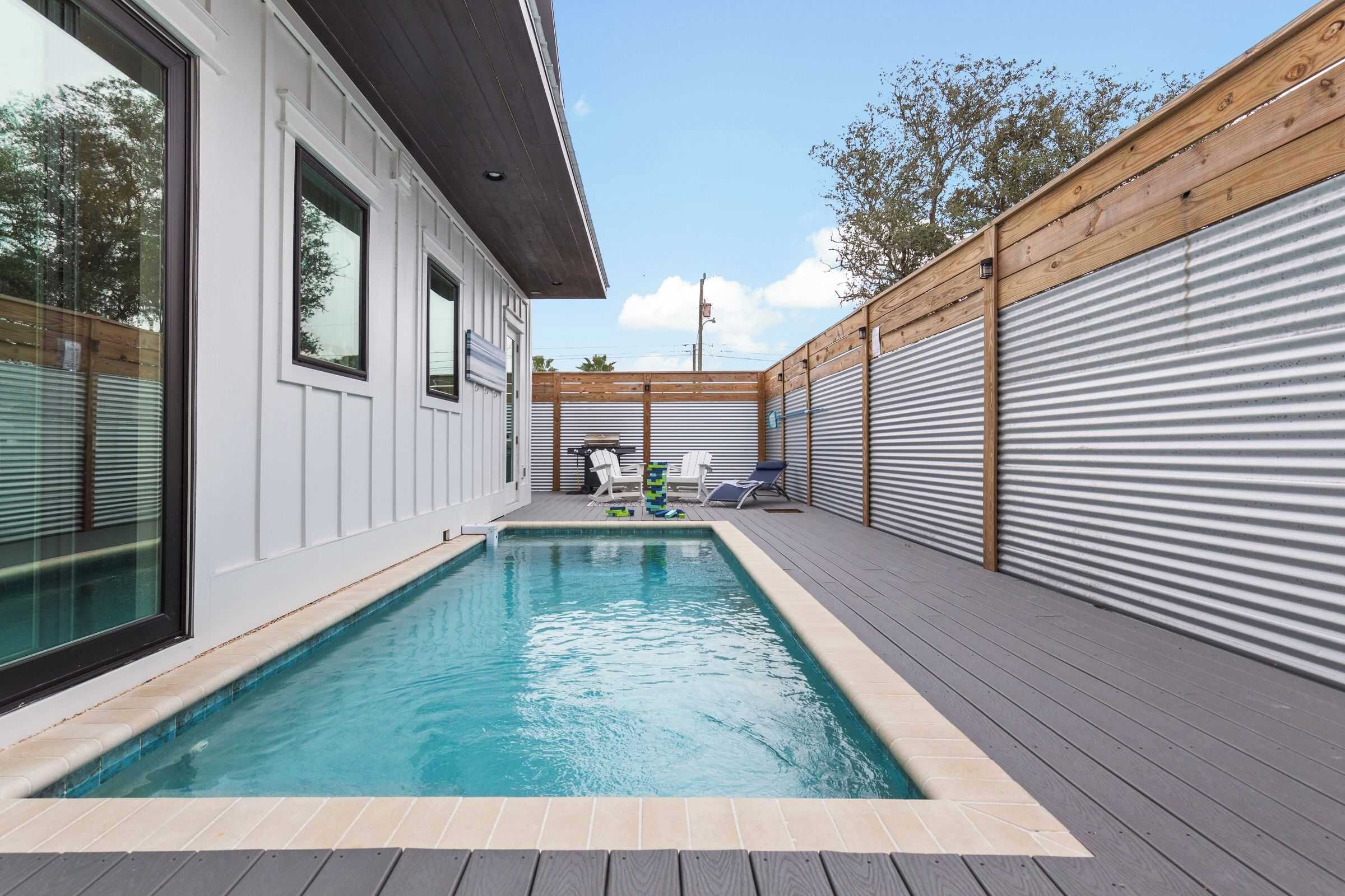 Ein moderner Poolbereich mit rechteckigem Pool, Holzdeck und einem Gebäude mit großen Fenstern.