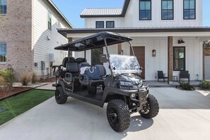 Een golfkarretje geparkeerd voor een modern huis met een bakstenen gevel en witte beplating.