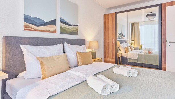 A hotel room with a large bed, a nightstand, a lamp, and a wardrobe. - NEW Greta - Your home in the magical Black Forest (Baiersbronn)