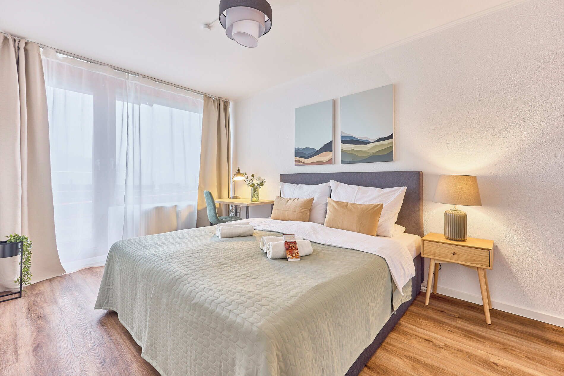 Une chambre d’hôtel avec un grand lit, une table de chevet avec une lampe, une chaise et une fenêtre avec des rideaux.