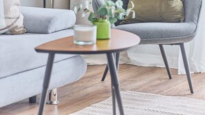 A modern living room with a grey armchair, a round wooden coffee table, a floor lamp, and a large window with curtains. - NEW Greta - Your home in the magical Black Forest (Baiersbronn)
