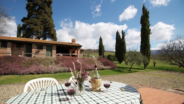 A table set outdoors with a checkered tablecloth, a bottle, and glasses, with a building and trees in the background.