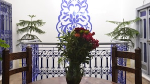 A table with a vase of flowers, a blue decorative wall, and a railing with plants. - Riad Wink (Marrakech)