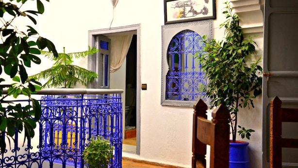 A courtyard with a blue wrought iron gate, a potted plant, and a wooden chair. - Riad Wink (Marrakech)