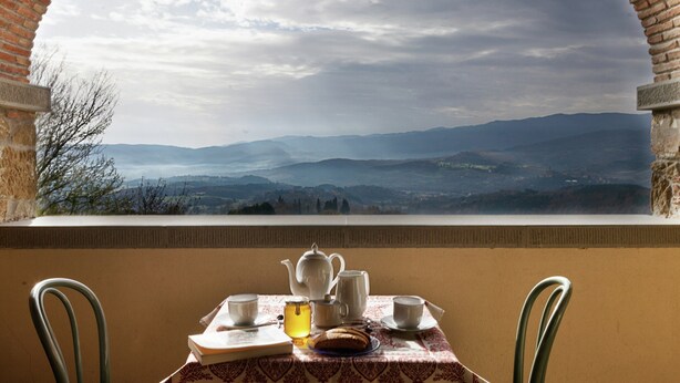 Une table dressée avec du thé et des pâtisseries, donnant sur un paysage montagneux à travers une fenêtre en arc de cercle.