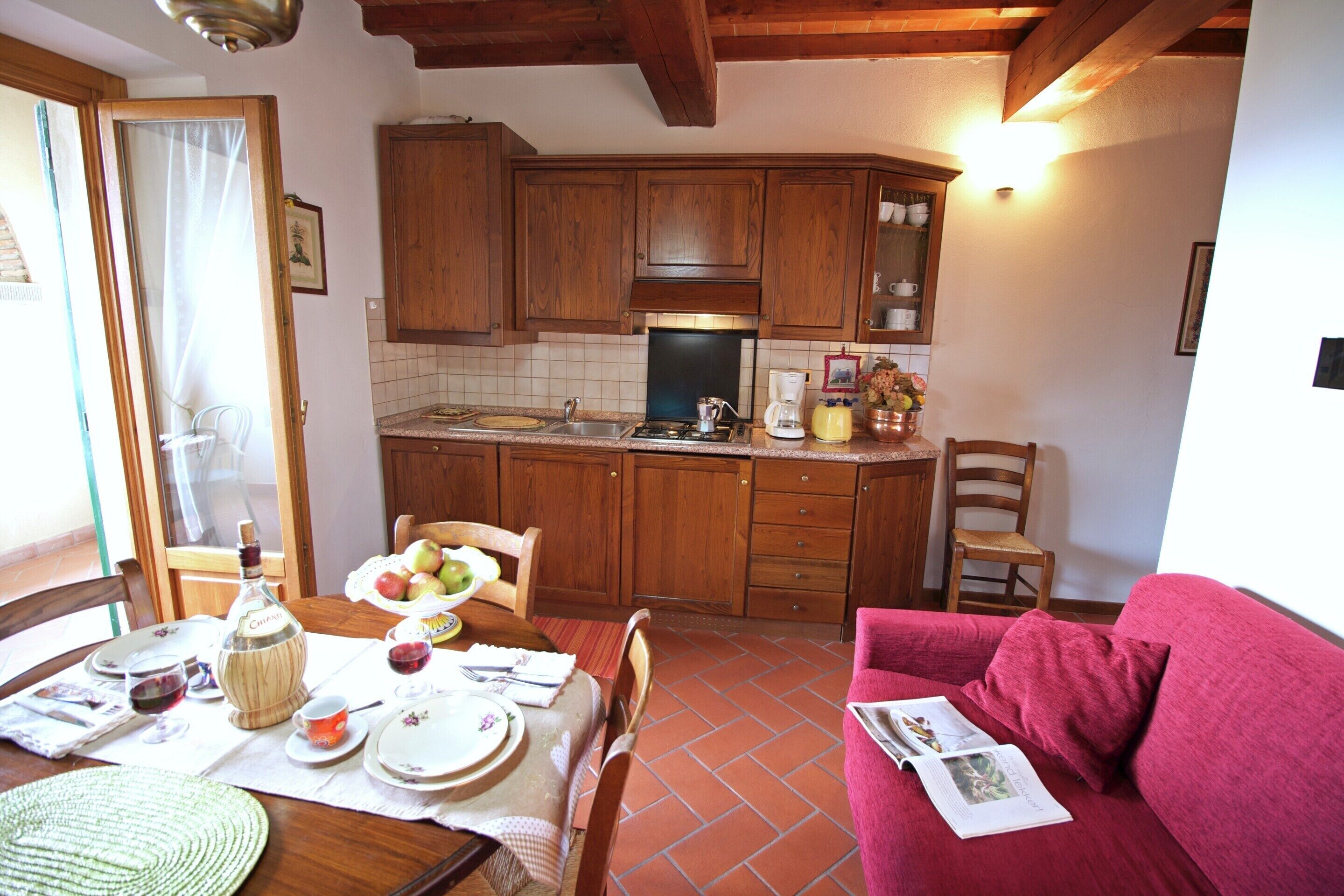 A cozy kitchen with wooden cabinets, a dining table set with plates, glasses, and a bottle.