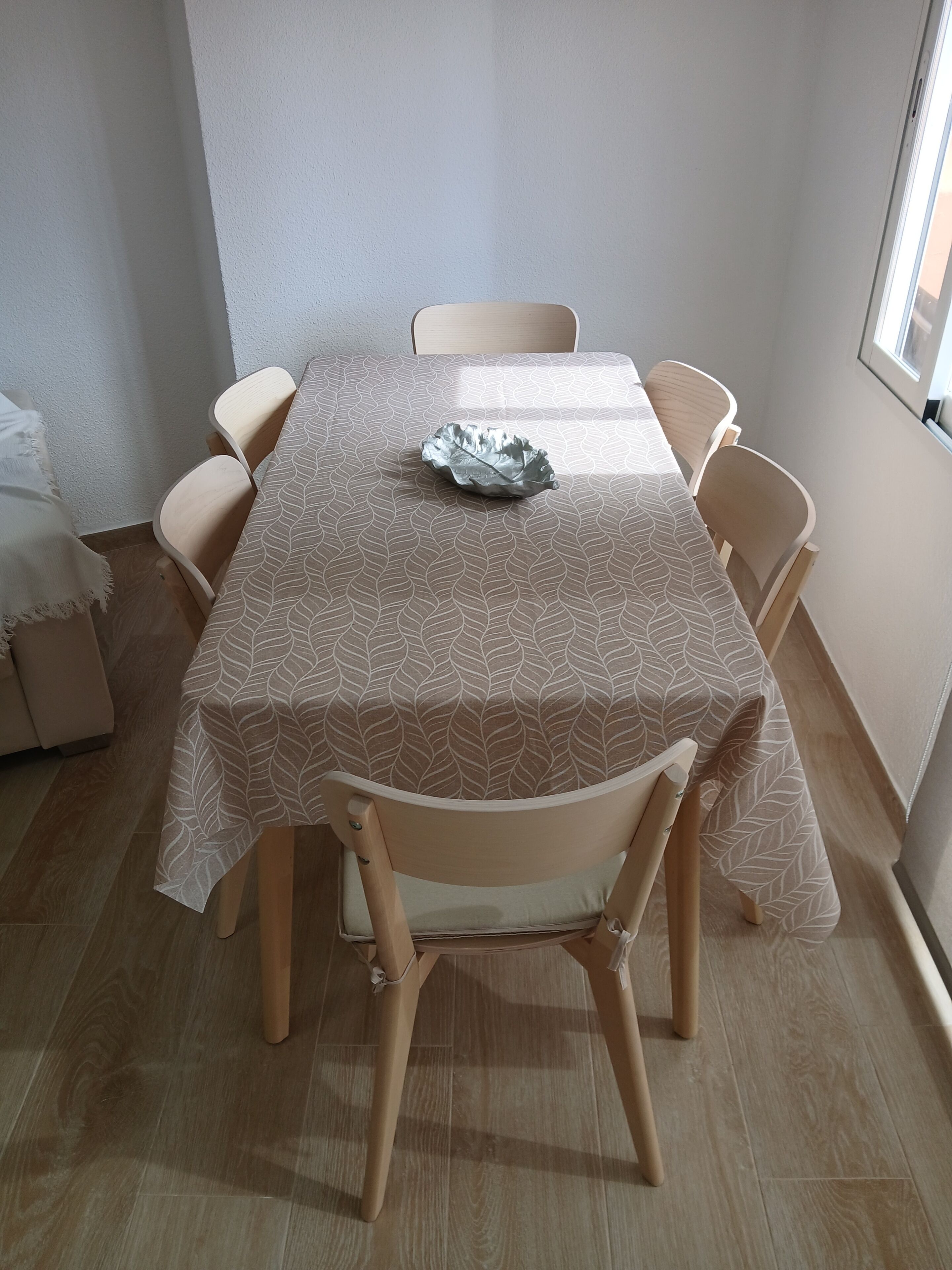 Una mesa de comedor con mantel estampado de hojas, rodeada de seis sillas de madera.