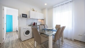 A compact kitchen with a washing machine, a microwave, and a dining area with a glass table and chairs. - Apartamentos Chorrol (Benidorm)