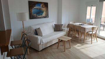 Een moderne woonkamer met een witte bank, een klein bijzettafeltje, en een eethoek met houten stoelen en een tafel.