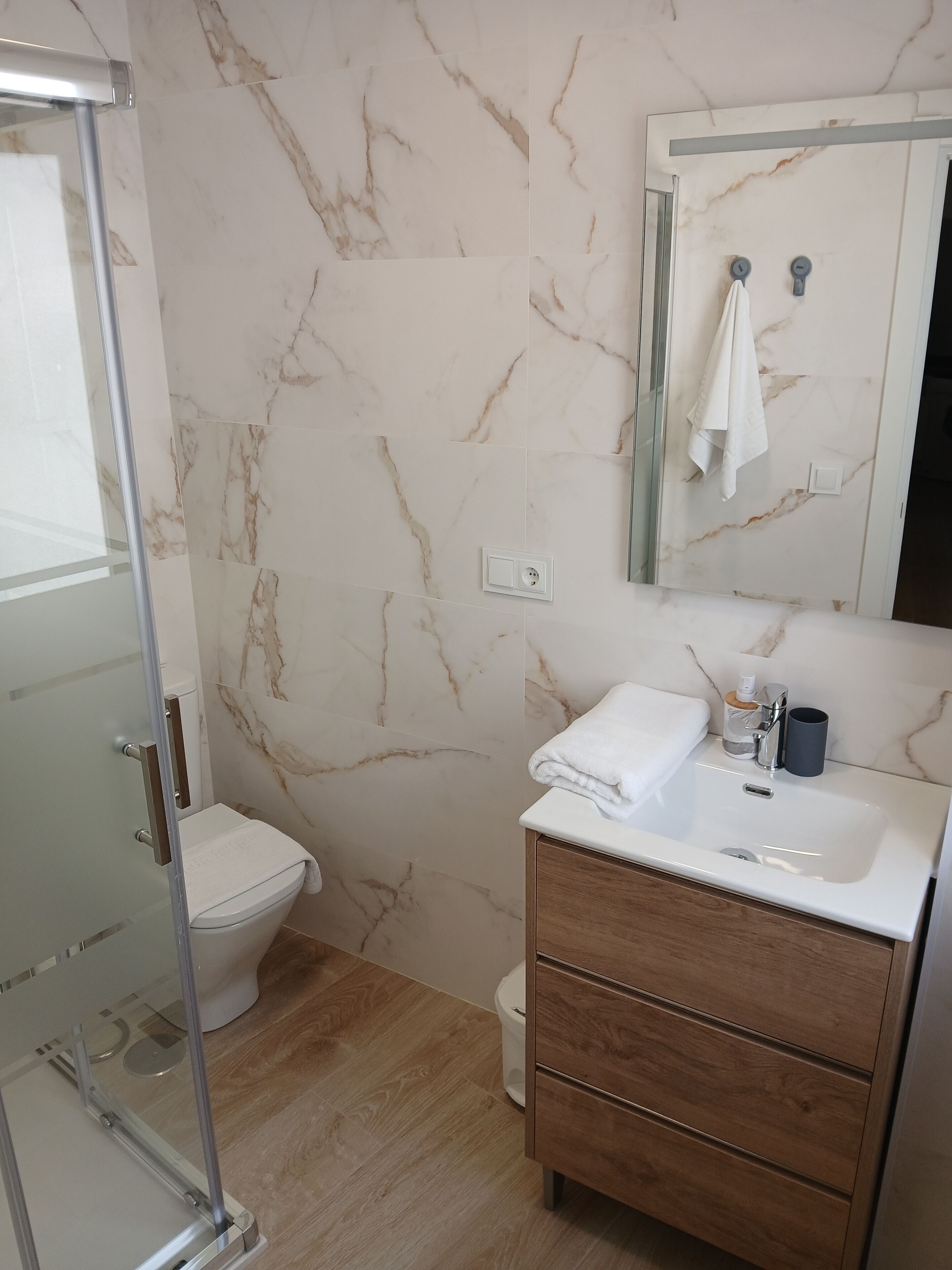 A modern bathroom with a glass shower enclosure, a toilet, a vanity with a mirror, and a sink.