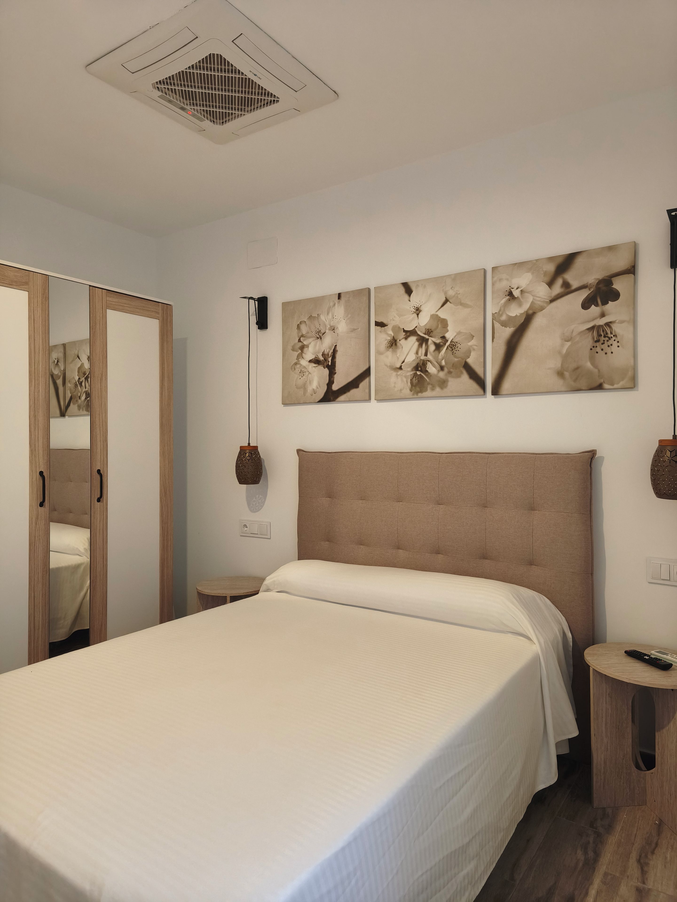 A bedroom with a large bed, a wardrobe, a mirror, and wall-mounted artwork.