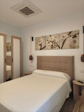 A bedroom with a large bed, a wardrobe, a mirror, and wall-mounted artwork. - Apartamentos Chorrol (Benidorm)