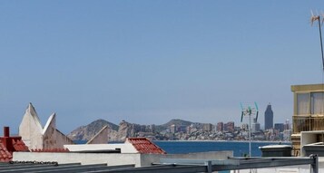 Un paysage urbain côtier, avec un bâtiment imposant au premier plan et une chaîne de montagnes en arrière-plan.