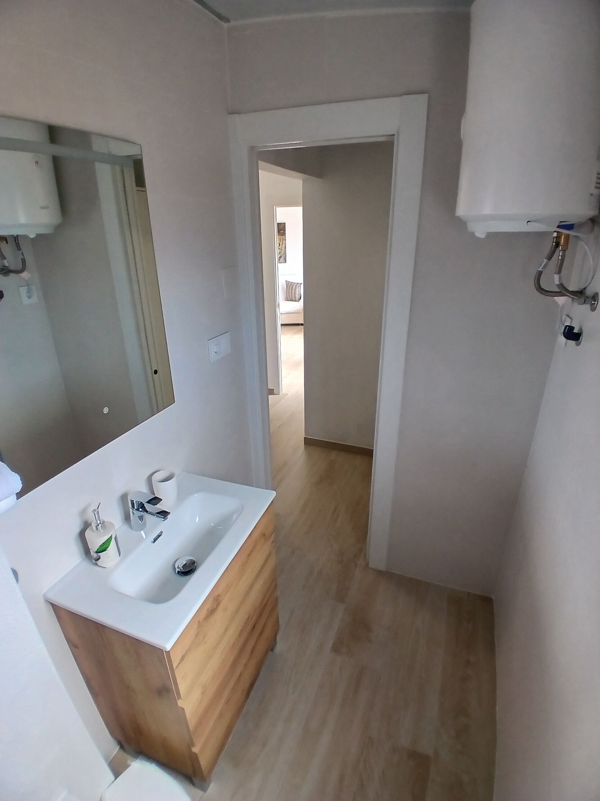 A modern bathroom with a wooden vanity, a large mirror, and a shower area.