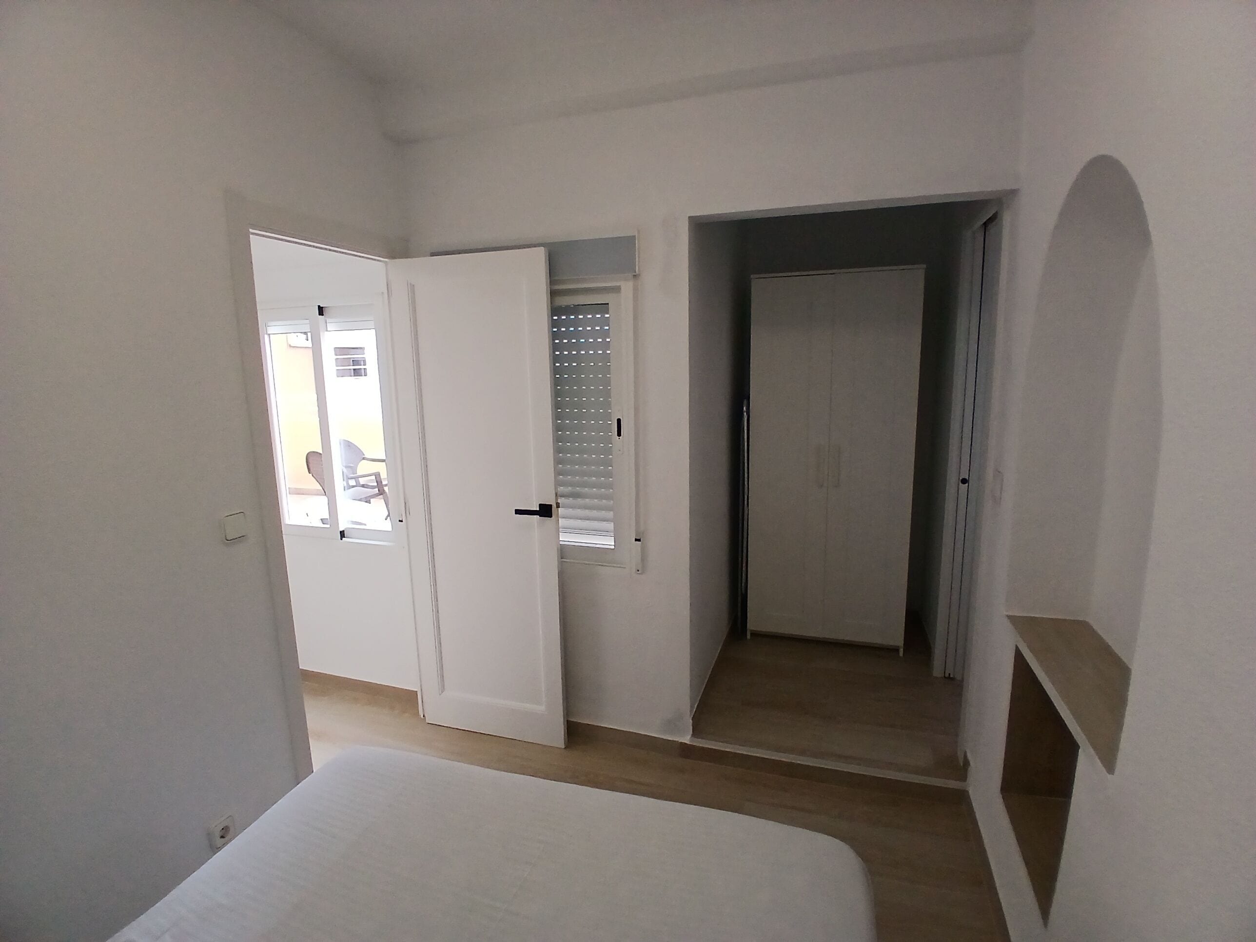 A bedroom with a bed, a door leading to a balcony, and a door to a hallway.