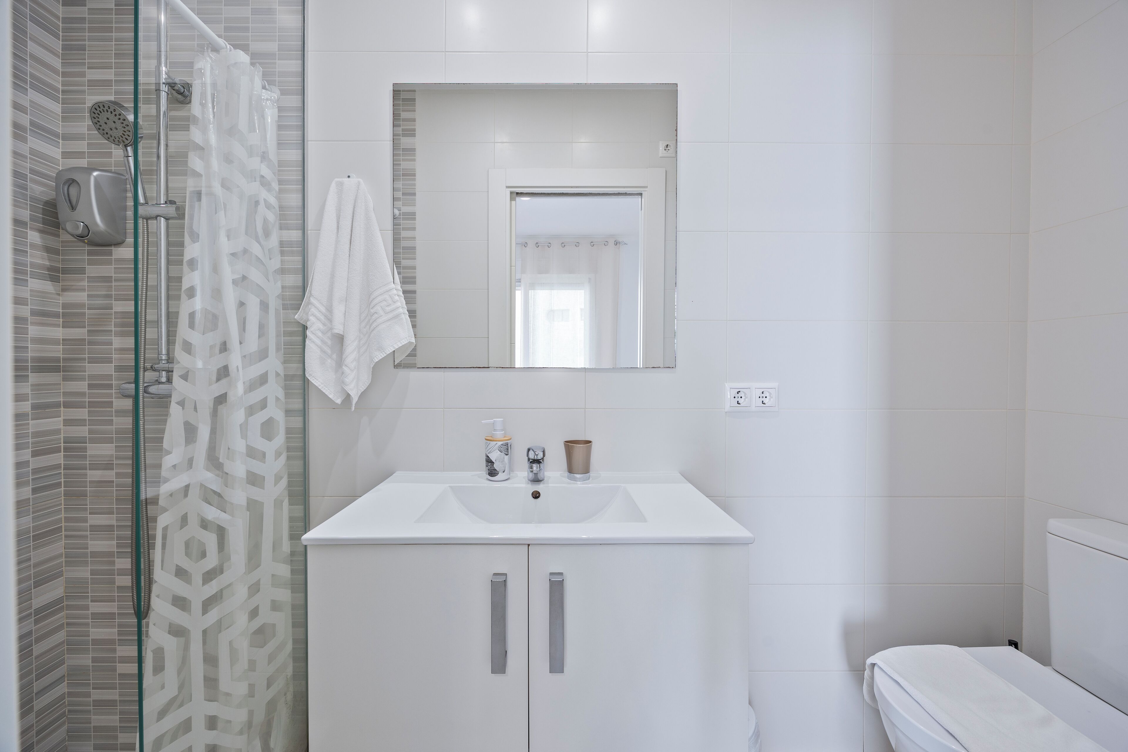 A bathroom with a shower, a sink with a mirror, and a toilet.