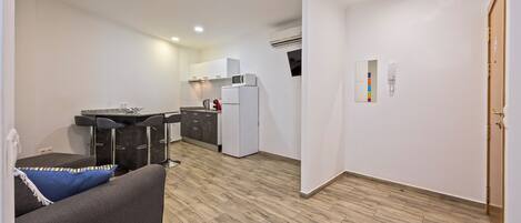 A modern kitchen with white cabinets, a refrigerator, and a microwave. There is a bar area with stools and a countertop.