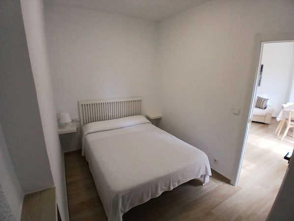Una habitación pequeña y limpia con una cama individual, una mesita de noche y una silla.