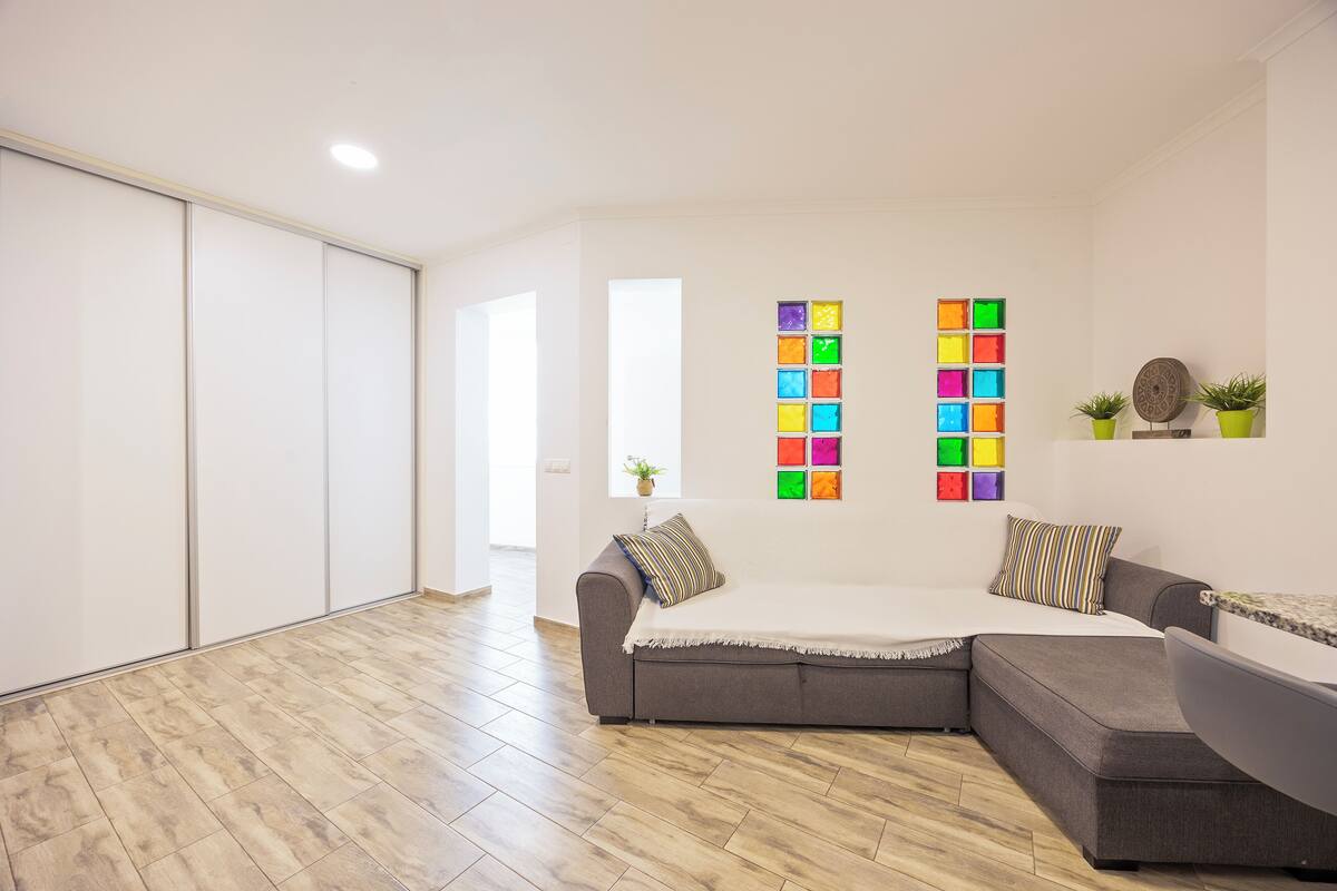 A modern living room with a sectional sofa, a small table, and a colorful wall art installation.