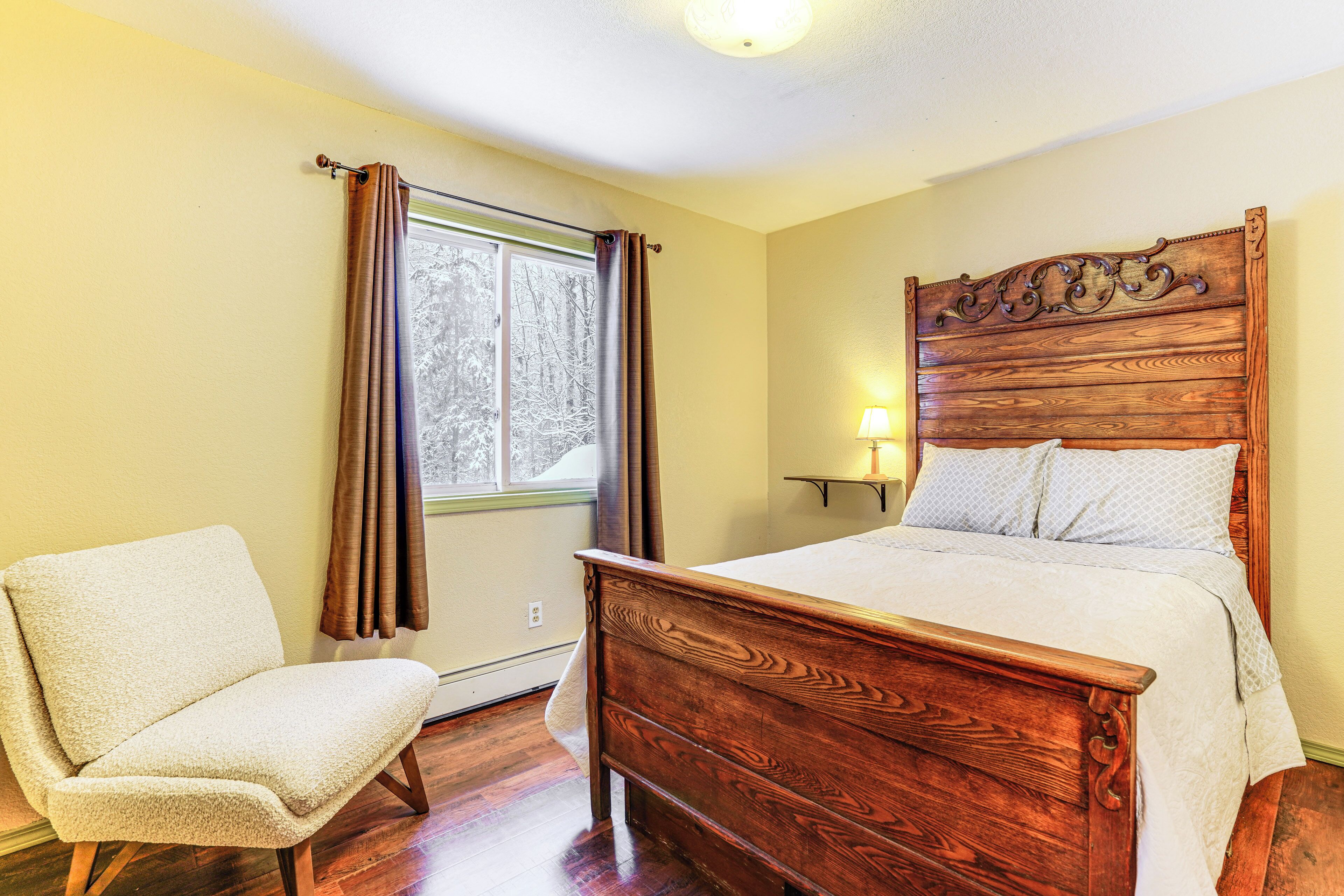 A bedroom with a wooden bed, a chair, and a window with curtains.