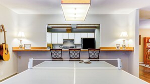 A dining area with a ping pong table, three chairs, a guitar, and a kitchen in the background. - Home 20 Mi to Anchorage & Chugach State Park! (Chugiak)