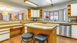 A modern kitchen with wooden cabinetry, a central island with stools, a dishwasher, and a window providing a view. - Home 20 Mi to Anchorage & Chugach State Park! (Chugiak)
