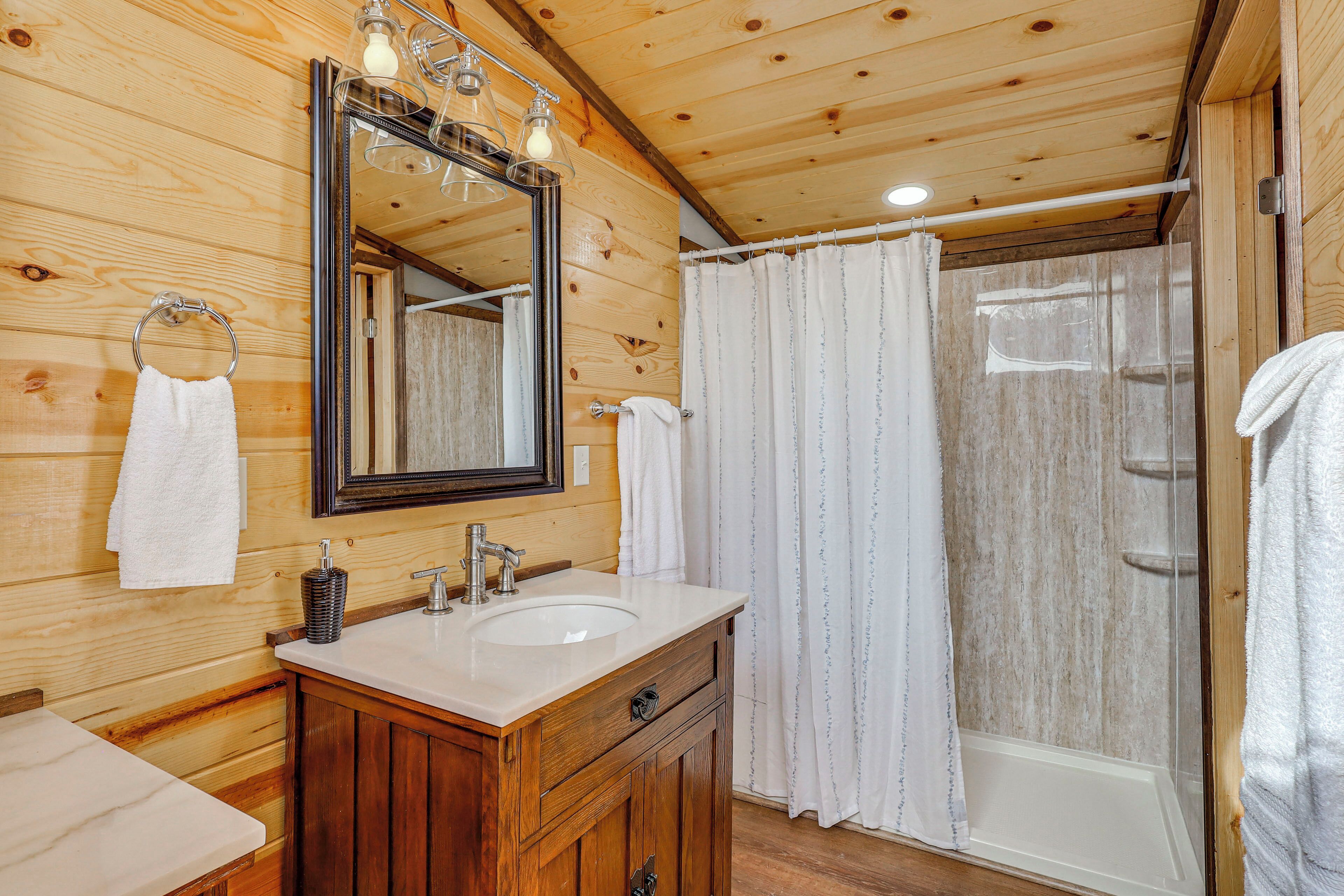 A wooden cabin bathroom with a wooden vanity, a sink, a mirror, and a shower with a curtain.