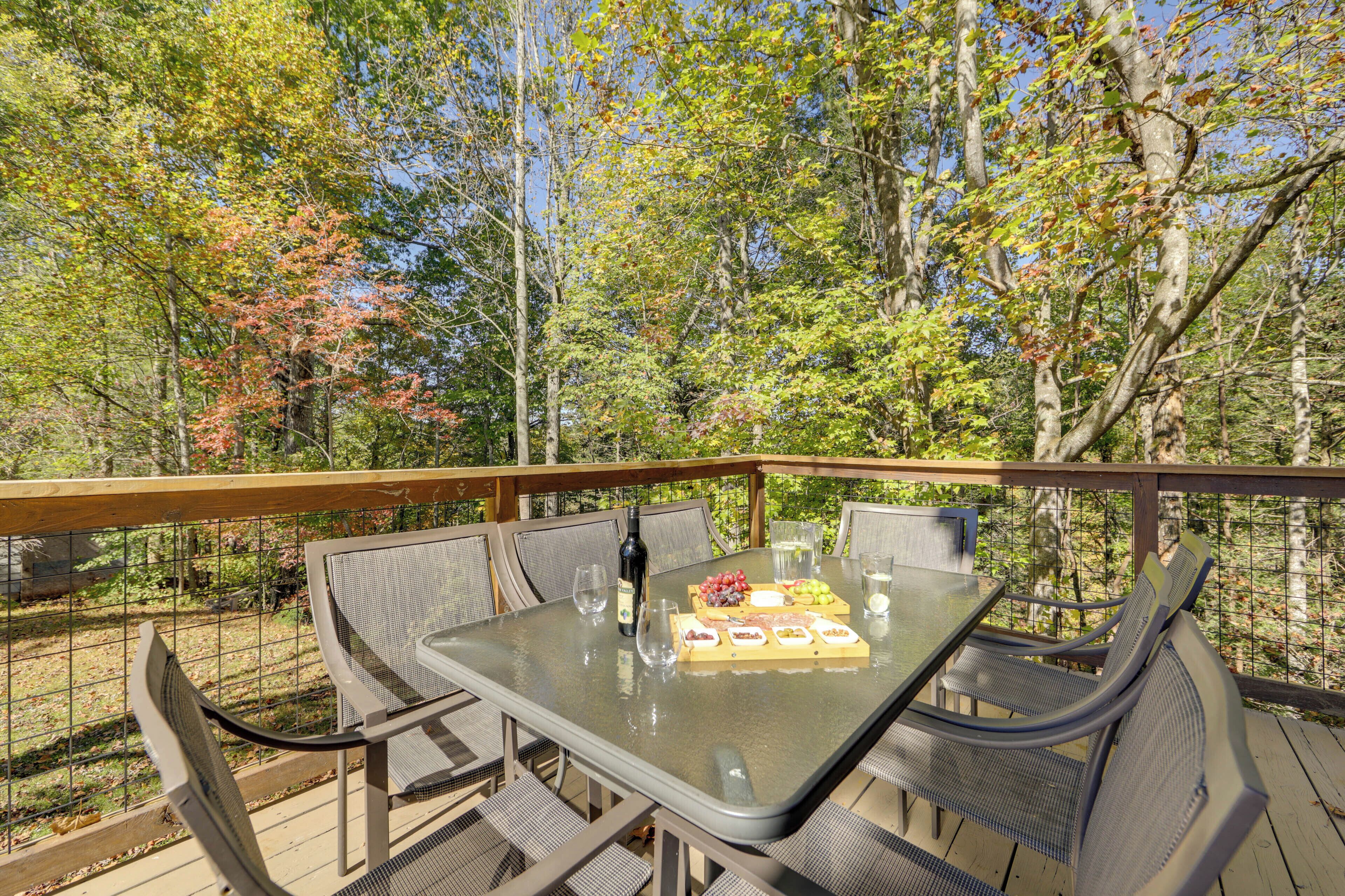 An outdoor dining area with a table set for four, surrounded by wicker chairs, overlooking a forested area.