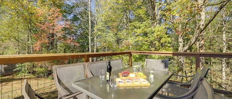 An outdoor dining area with a table set for four, surrounded by wicker chairs, overlooking a forested area.