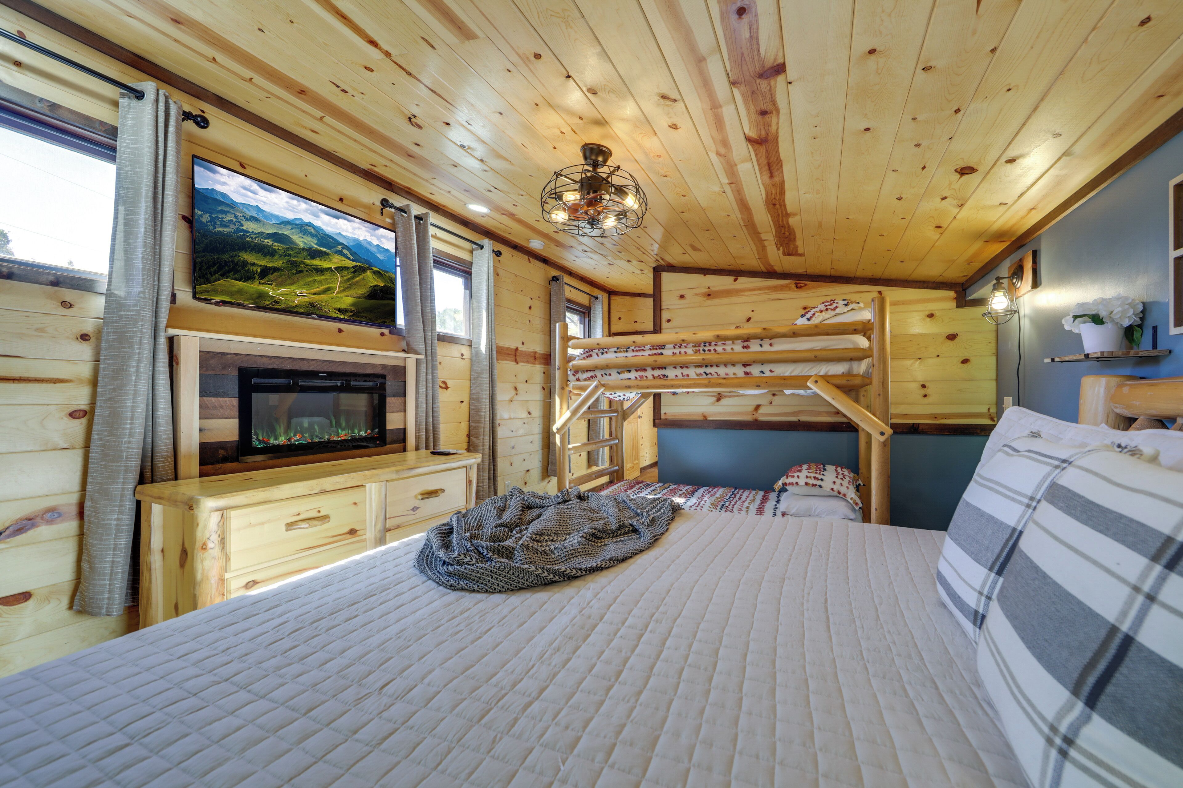 Un acogedor interior de cabaña con literas, chimenea, televisión y una vista panorámica a través del ventanal.