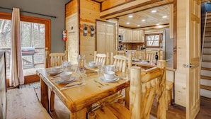 A wooden dining area with a table set for four, a kitchen in the background, and a door leading to another room.