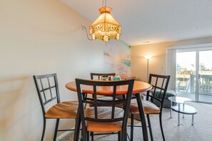A dining area with a round table, four chairs, a hanging light fixture, and a view through a glass door to the outside.