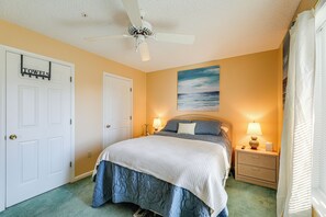 A bedroom with a bed, a nightstand, a ceiling fan, a door, and a painting on the wall.