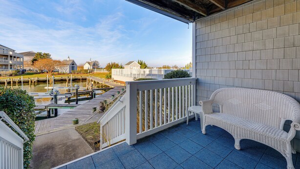 A balcony with a white wicker sofa and a white railing overlooking a marina with boats and a dock. - Half Mi to Beach: Bayfront Ocean City Condo, Deck (Ocean City)