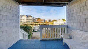 A covered balcony with a white wicker sofa and a view of a marina with boats and buildings. - Half Mi to Beach: Bayfront Ocean City Condo, Deck (Ocean City)