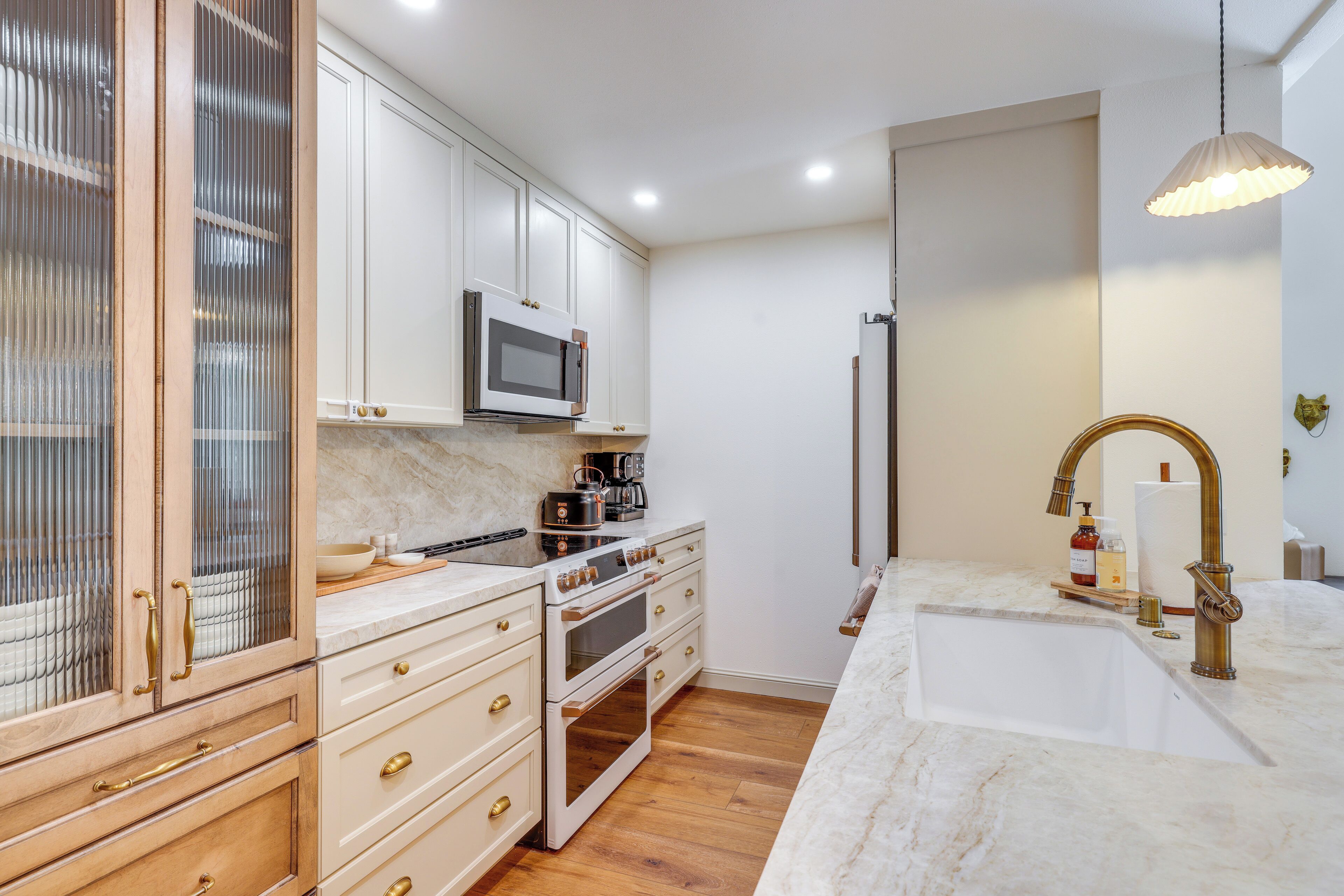 A modern kitchen with white cabinets, a built-in microwave, a stainless steel range, and a marble countertop.