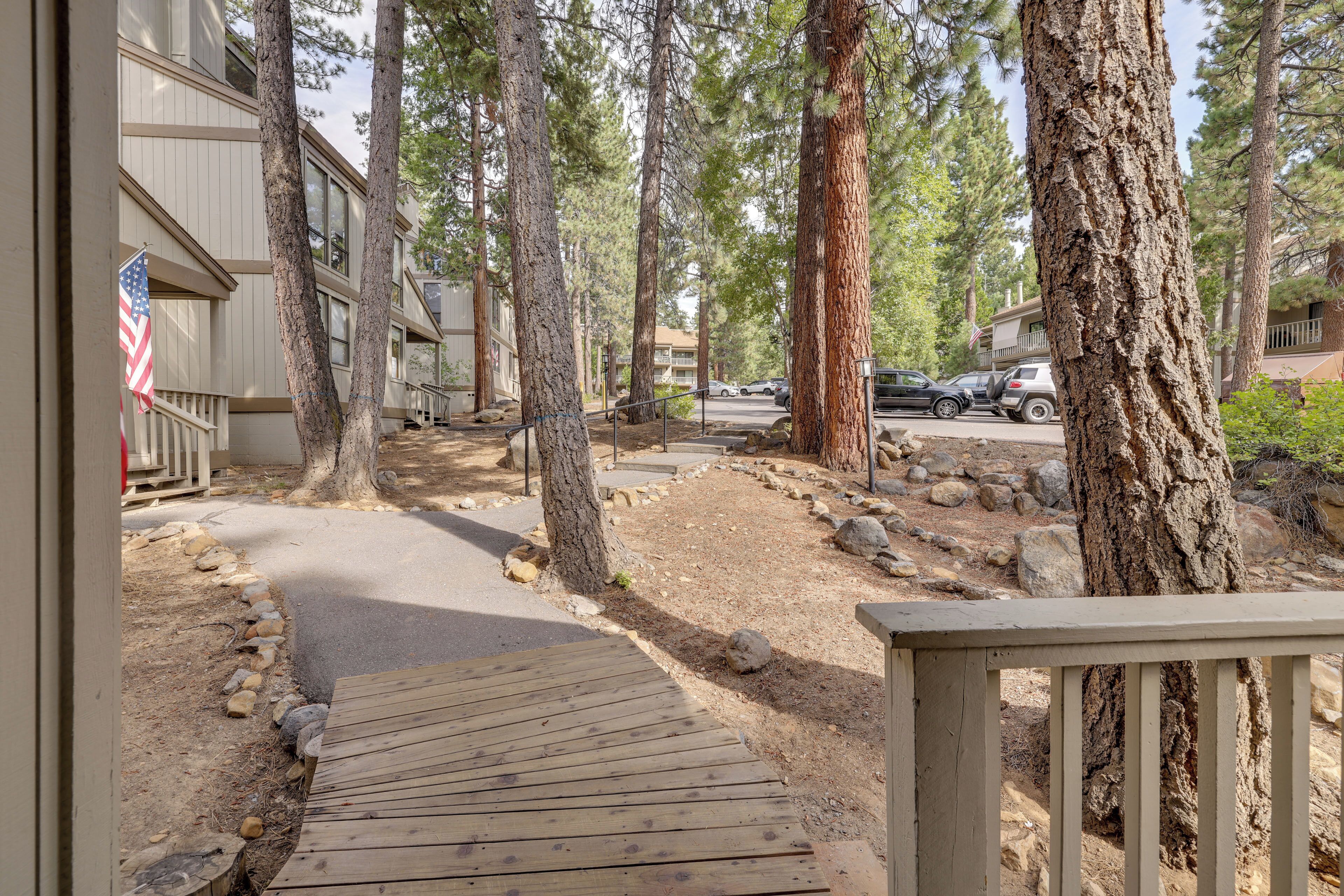 A wooden deck leading to a building with a flag, surrounded by trees and a parking area.