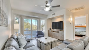 Un salon moderne avec un canapé d’angle gris, une table basse, un ventilateur de plafond, un téléviseur et une porte coulissante donnant sur un balcon.