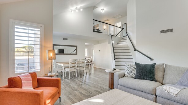 Un vaste espace de vie comprenant un canapé, une table basse et une table à manger avec des chaises. Un escalier mène à l’étage supérieur.