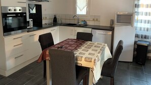 A compact kitchen with a stove, microwave, and dishwasher. There is a dining table with four chairs and a patterned tablecloth. - Peaceful accommodation 2 steps from amenities  (L'Isle-sur-la-Sorgue)