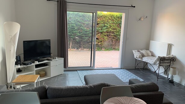 A modern living room with a flat-screen TV, a sofa, a chair, and a view through a sliding glass door to an outdoor area. - Peaceful accommodation 2 steps from amenities  (L'Isle-sur-la-Sorgue)