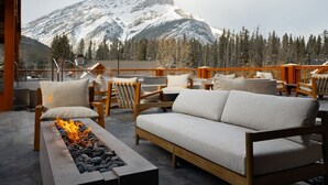A cozy outdoor seating area with a fire feature, wooden furniture, and a mountain view. - Queen Beds in Spacious Superior Room in Banff (Banff)
