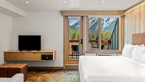 Una camera d'albergo con un letto grande, una TV su un mobile in legno, un tappeto colorato e vista sulle montagne dalle finestre.