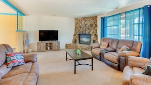 A living room with leather sofas, a stone fireplace, a flat-screen TV, and a blue curtain. - 11 Mi to Skiing: Valdez Home w/ Mtn Views! (Arroyo Seco)