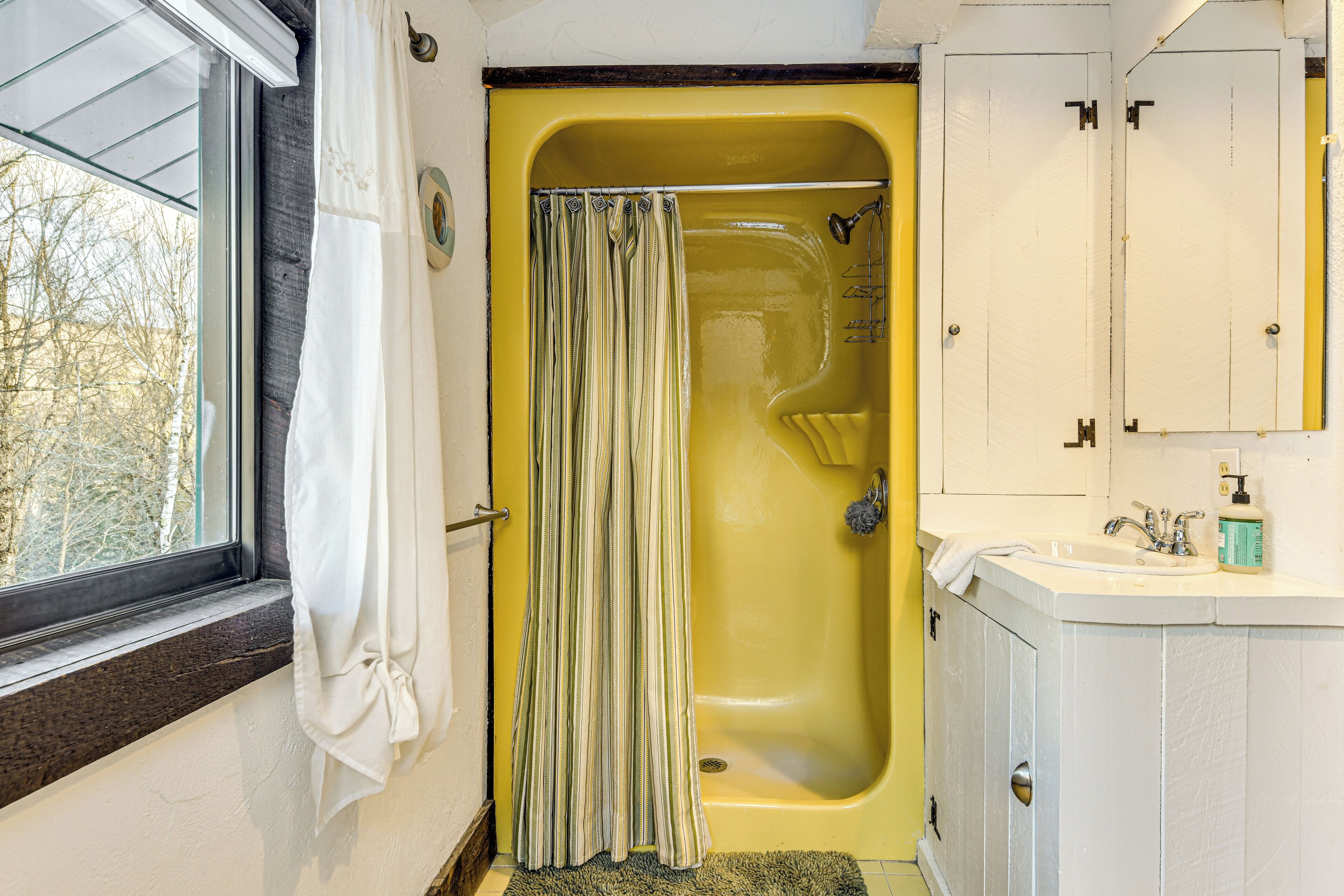A bathroom with a yellow bathtub, a white sink, and a window with a white curtain.