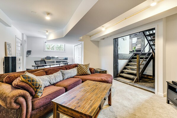 A spacious living room with a large sectional sofa, a wooden coffee table, and a staircase leading to an upper floor. - 11 Mi to Sugarbush: Eclectic Ski House w/ Hot Tub! (Roxbury)