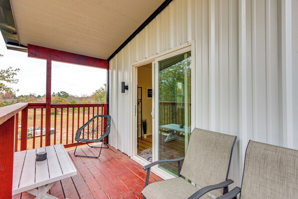 A covered porch with a table and two chairs, a sliding glass door leading to an outdoor area, and a red railing. - Hike & Explore: 60-acre Outdoor Retreat in Tyler! (Tyler)