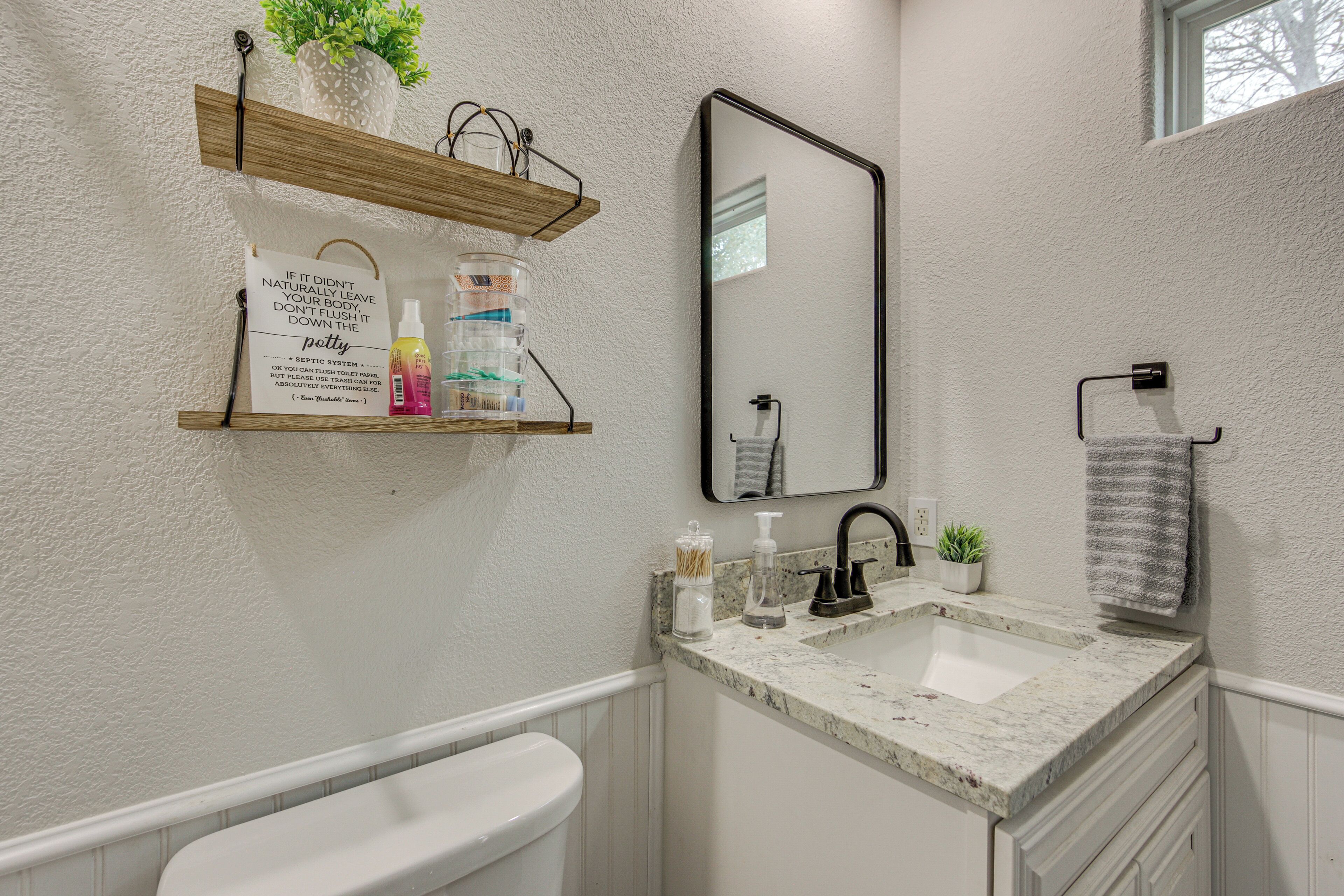 A bathroom with a toilet, a sink with a mirror, a towel rack, and a shelf with toiletries.