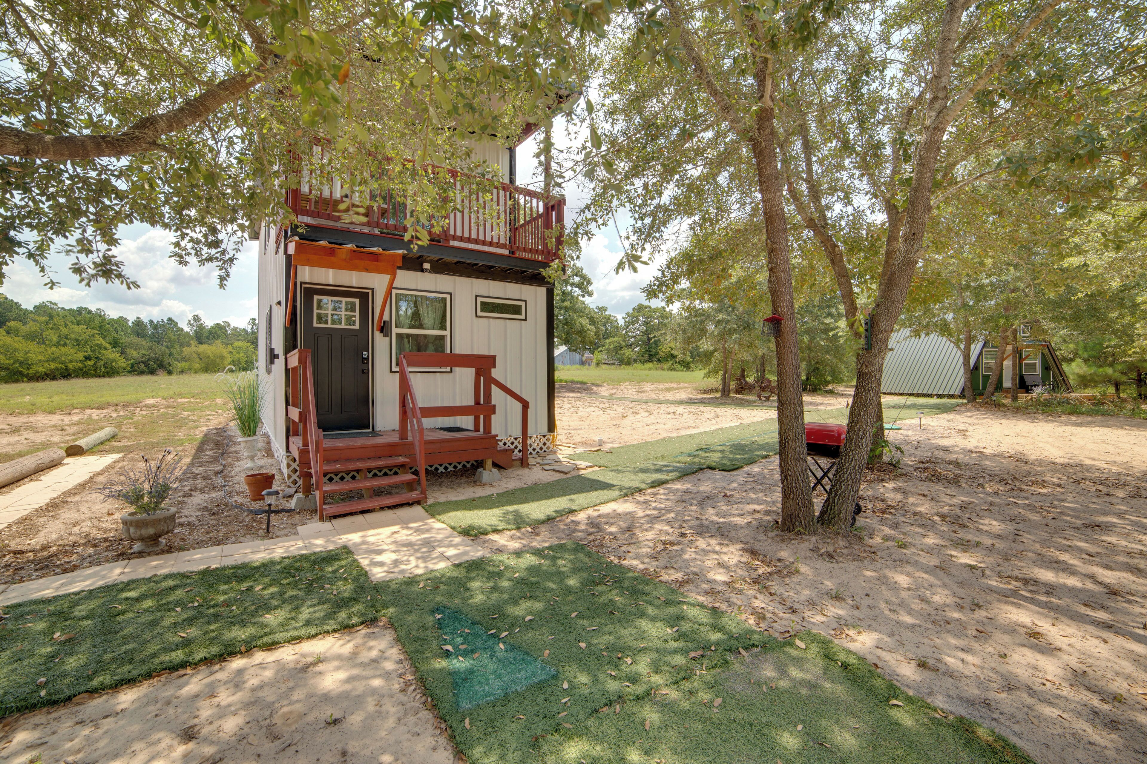 A small cabin with a porch, surrounded by trees and a grassy yard.